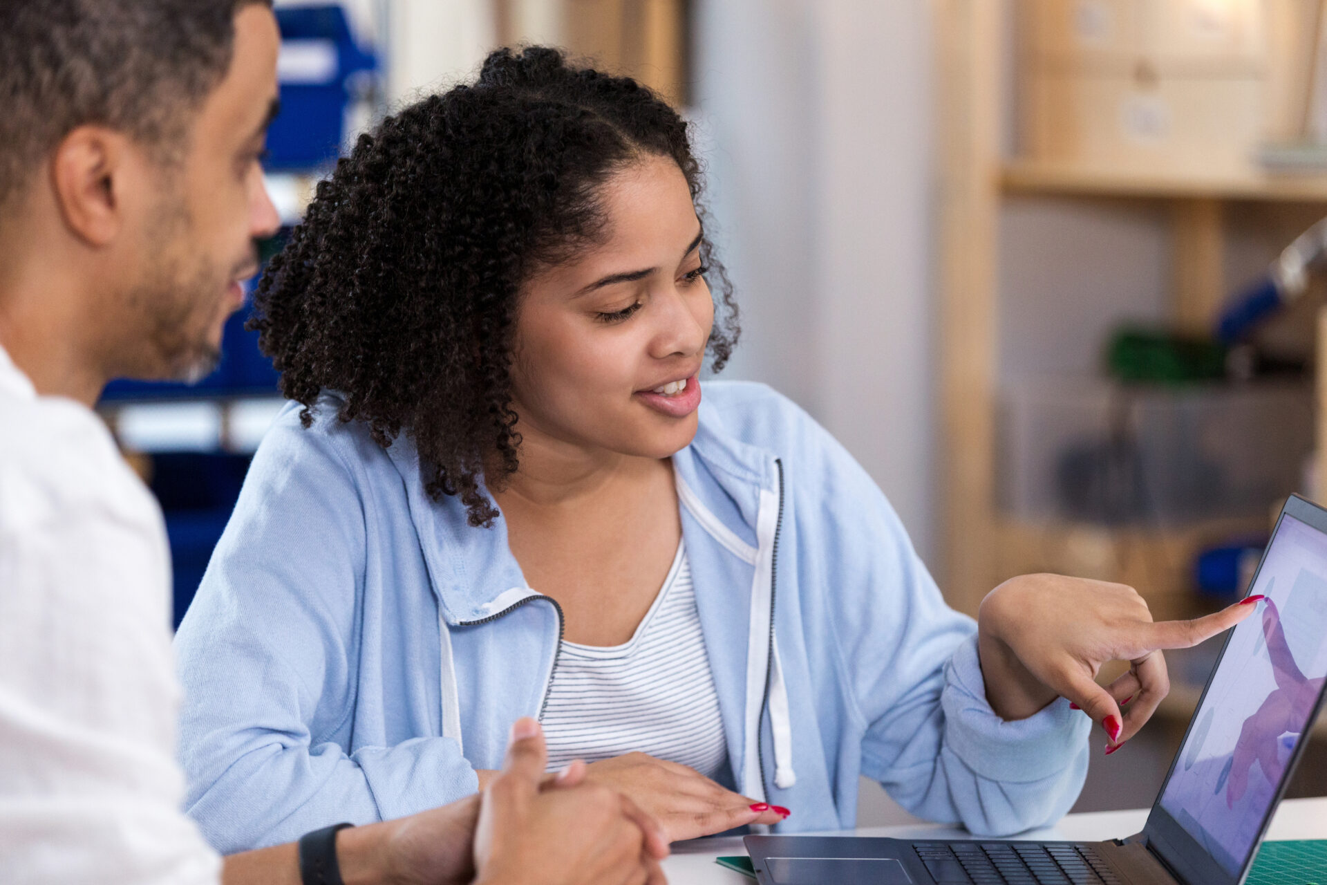 Confident cute teenage girl points to something on laptop screen while talking to her dad. Her dad is helping with a homework assignment.